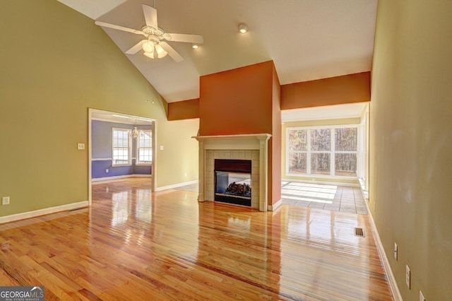 unfurnished living room featuring high vaulted ceiling, ceiling fan, a tile fireplace, and light hardwood / wood-style flooring