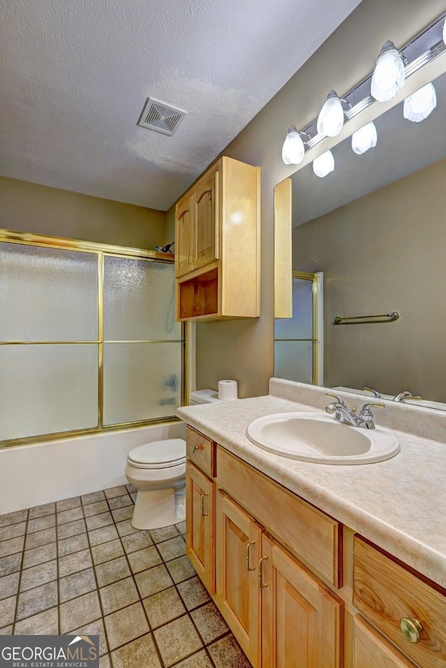 full bathroom with combined bath / shower with glass door, tile patterned floors, vanity, a textured ceiling, and toilet