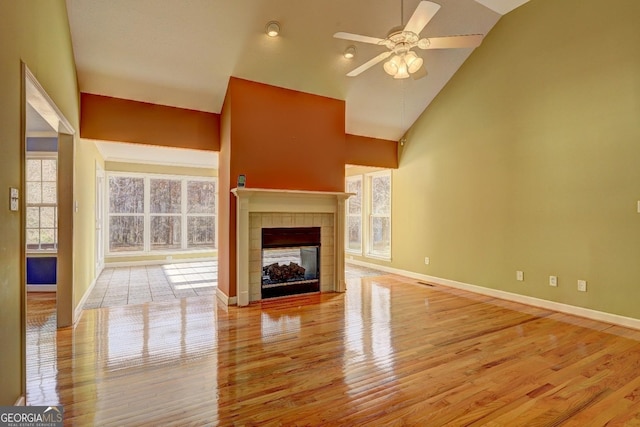 unfurnished living room featuring ceiling fan, light wood-type flooring, a fireplace, and high vaulted ceiling