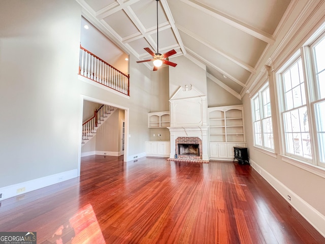 unfurnished living room featuring beamed ceiling, a brick fireplace, built in features, hardwood / wood-style flooring, and ceiling fan