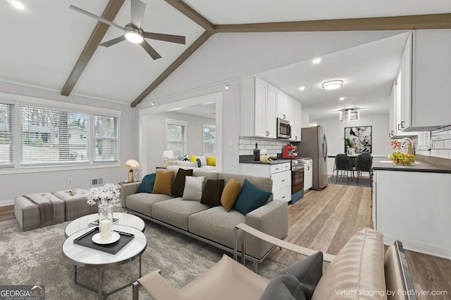 living room featuring lofted ceiling with beams, light hardwood / wood-style floors, ceiling fan, and a healthy amount of sunlight