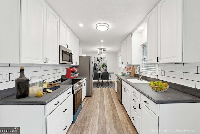 kitchen featuring white cabinetry, sink, stainless steel appliances, tasteful backsplash, and light hardwood / wood-style floors