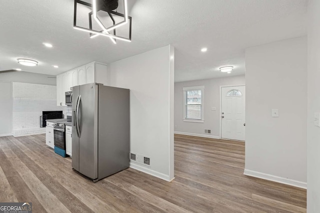 kitchen with white cabinets, stainless steel appliances, a textured ceiling, and light wood-type flooring