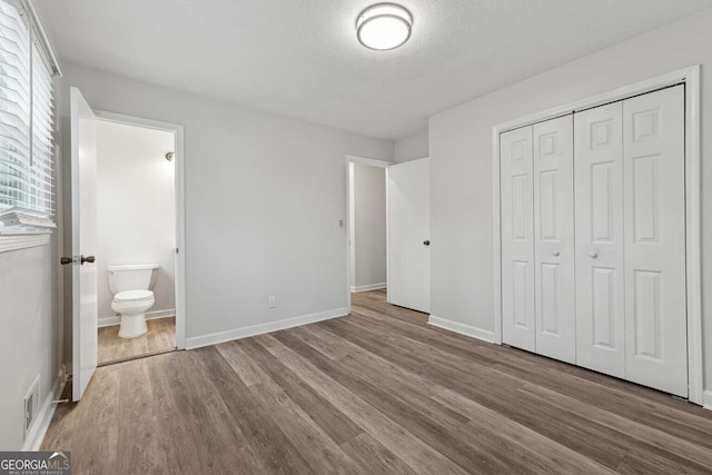 unfurnished bedroom featuring ensuite bathroom, wood-type flooring, a textured ceiling, and a closet