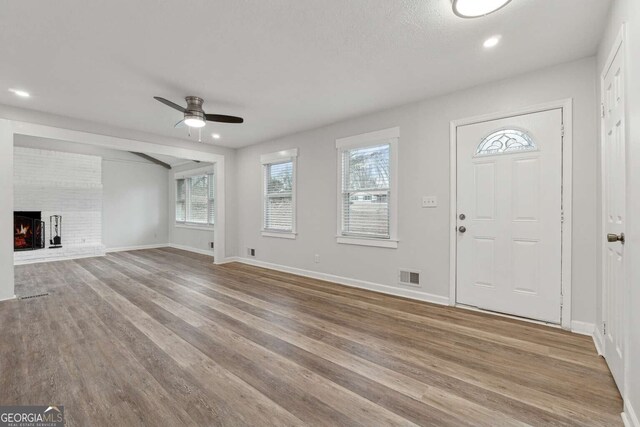 entrance foyer with light hardwood / wood-style flooring, a brick fireplace, and ceiling fan