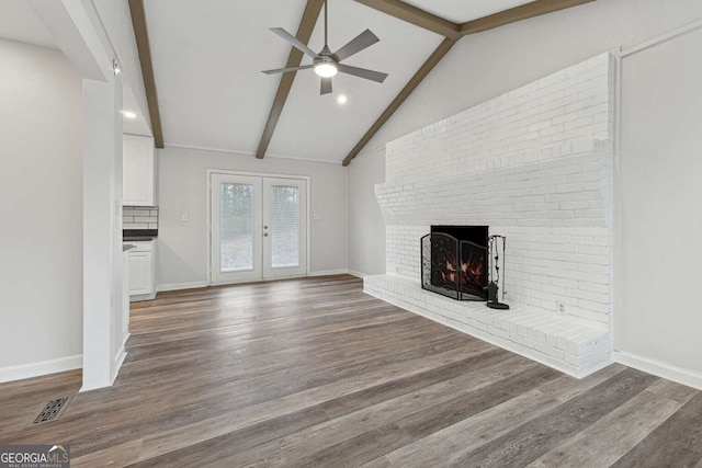 unfurnished living room with dark wood-type flooring, french doors, vaulted ceiling with beams, ceiling fan, and a fireplace