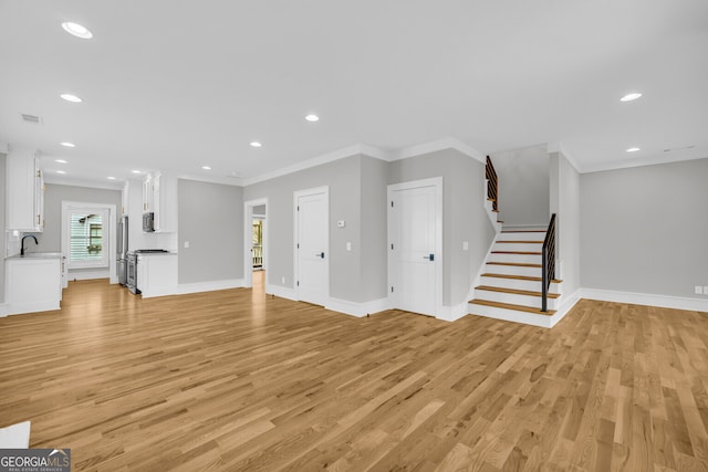 unfurnished living room featuring light hardwood / wood-style flooring, crown molding, and sink