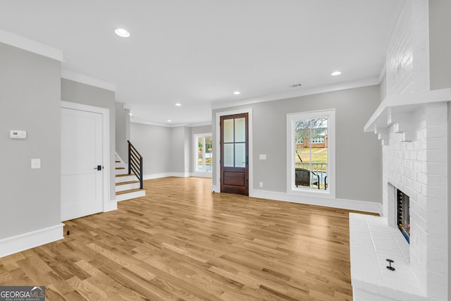 unfurnished living room featuring light wood-type flooring, crown molding, and a brick fireplace