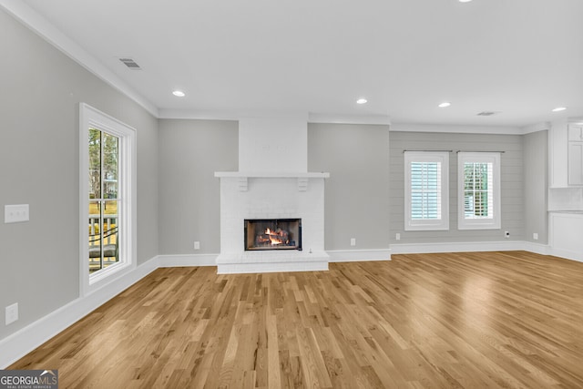 unfurnished living room featuring crown molding, light wood-type flooring, and a brick fireplace