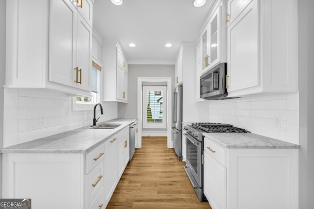 kitchen with appliances with stainless steel finishes, light wood-type flooring, light stone counters, sink, and white cabinetry