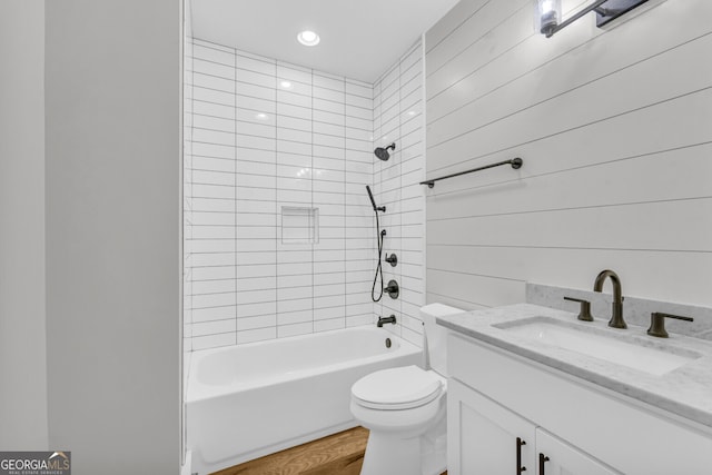 full bathroom featuring vanity, wooden walls, hardwood / wood-style flooring, toilet, and tiled shower / bath