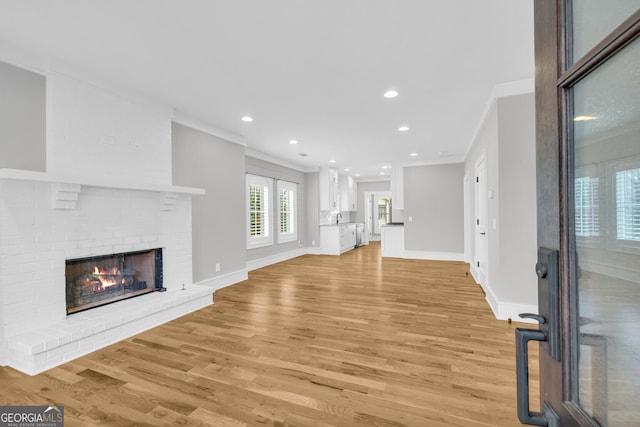 unfurnished living room with a brick fireplace, sink, light hardwood / wood-style floors, and ornamental molding