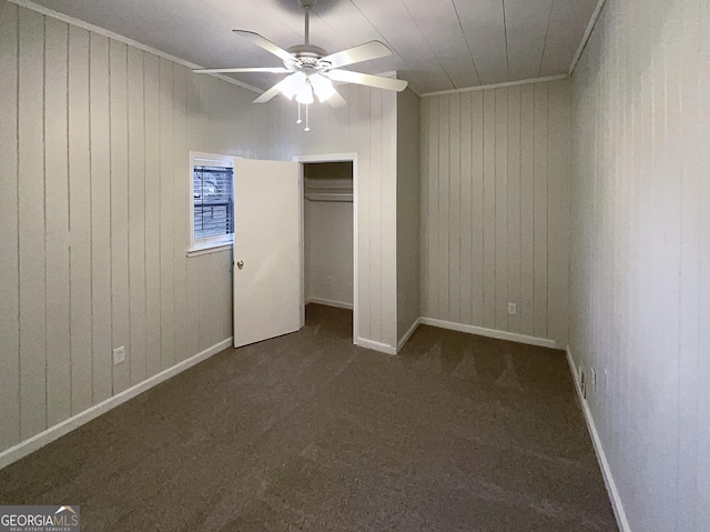 unfurnished bedroom featuring a closet, dark carpet, ceiling fan, and wood walls