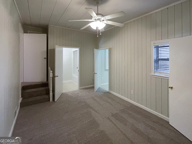 unfurnished bedroom featuring ceiling fan, wooden walls, and carpet