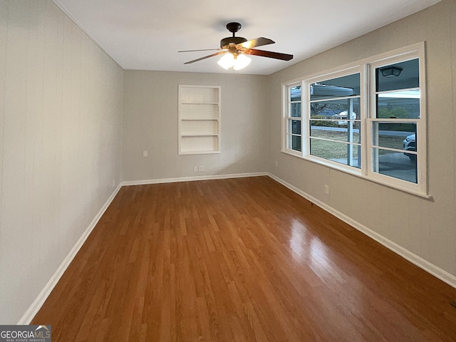 spare room with built in shelves, hardwood / wood-style flooring, and ceiling fan