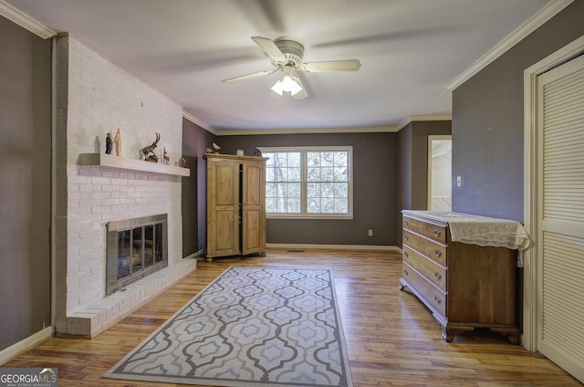 living room featuring a brick fireplace, light hardwood / wood-style flooring, ceiling fan, and ornamental molding