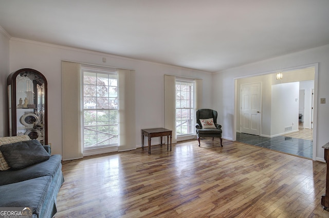 living area featuring baseboards, visible vents, crown molding, and wood finished floors