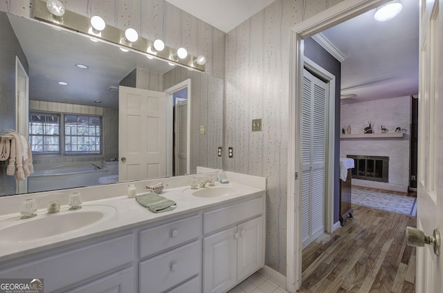 bathroom featuring wood-type flooring, vanity, a brick fireplace, a washtub, and crown molding