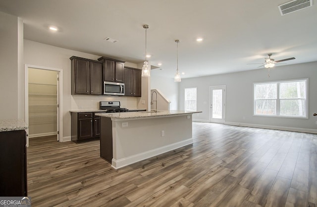 kitchen with dark wood-type flooring, appliances with stainless steel finishes, dark brown cabinets, and a center island with sink