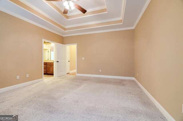 unfurnished bedroom featuring ensuite bathroom, a tray ceiling, ceiling fan, crown molding, and carpet floors