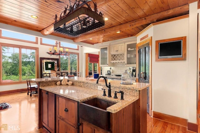 kitchen with an inviting chandelier, sink, light stone countertops, an island with sink, and light hardwood / wood-style floors