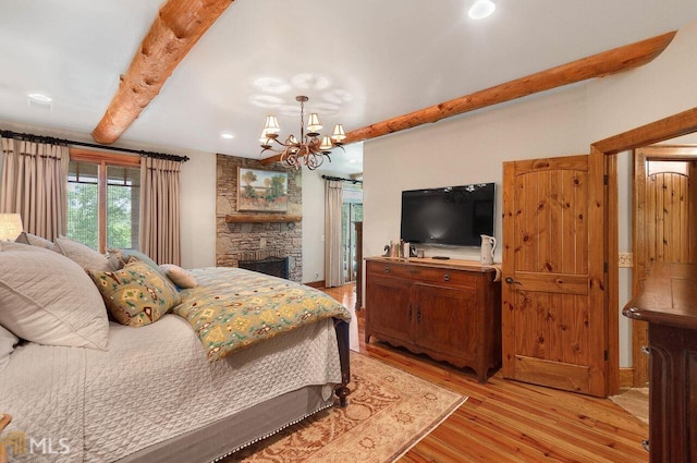 bedroom with beam ceiling, a stone fireplace, light wood-type flooring, and an inviting chandelier