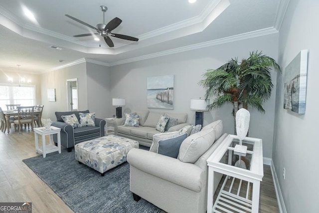 living room with a raised ceiling, crown molding, wood-type flooring, and ceiling fan with notable chandelier