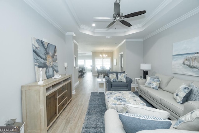 living room featuring ceiling fan with notable chandelier, light hardwood / wood-style flooring, a raised ceiling, and crown molding