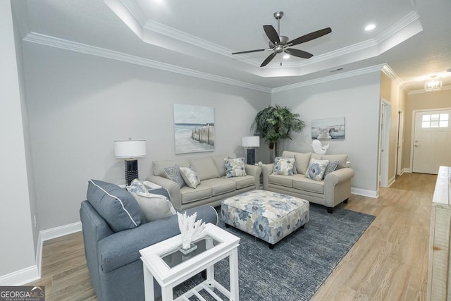 living room with ceiling fan, a raised ceiling, wood-type flooring, and crown molding