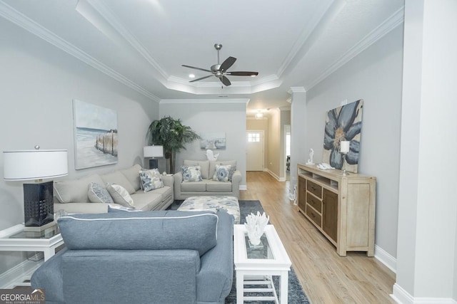 living room with light hardwood / wood-style floors, a raised ceiling, ceiling fan, and ornamental molding