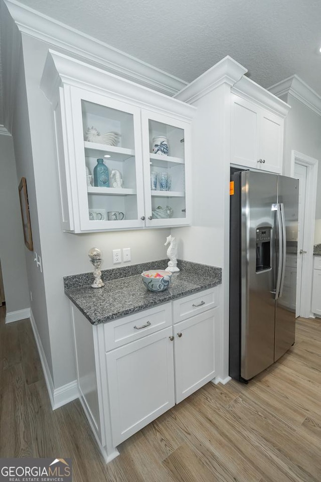 kitchen featuring stainless steel refrigerator with ice dispenser, dark stone counters, ornamental molding, light hardwood / wood-style flooring, and white cabinetry