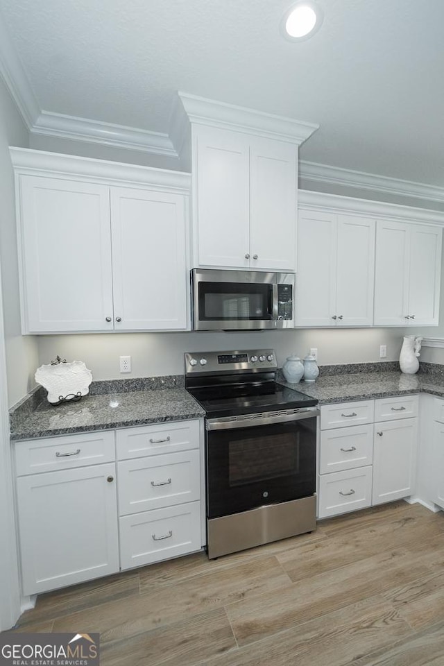 kitchen featuring appliances with stainless steel finishes, light wood-type flooring, white cabinetry, and ornamental molding