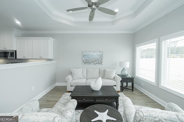 living room with light wood-type flooring, crown molding, and a tray ceiling