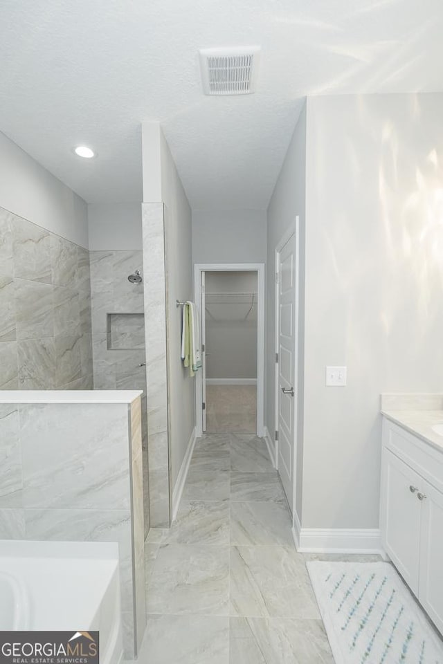 bathroom with a tile shower, vanity, and a textured ceiling