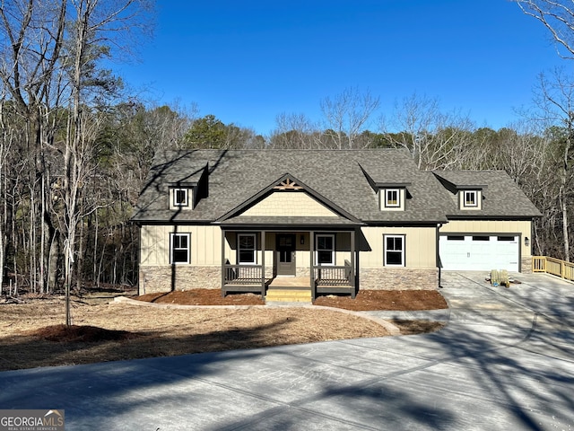 view of front of home with concrete driveway, roof with shingles, covered porch, a garage, and stone siding