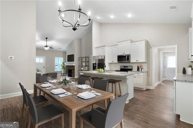 dining space featuring dark wood-style floors, visible vents, a fireplace, and high vaulted ceiling