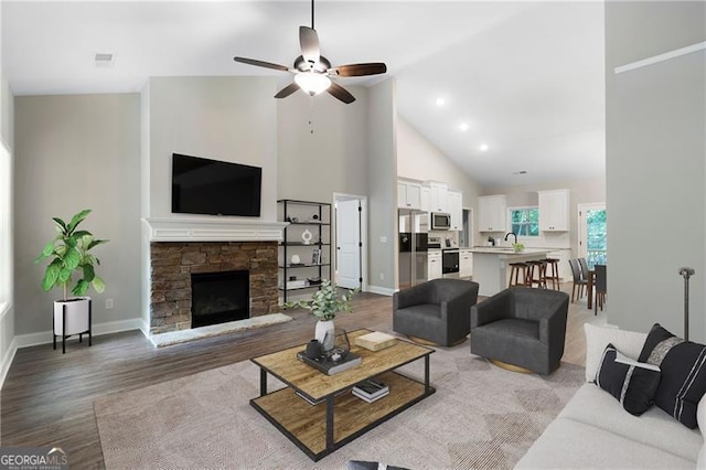 living room with visible vents, high vaulted ceiling, a stone fireplace, light wood finished floors, and baseboards