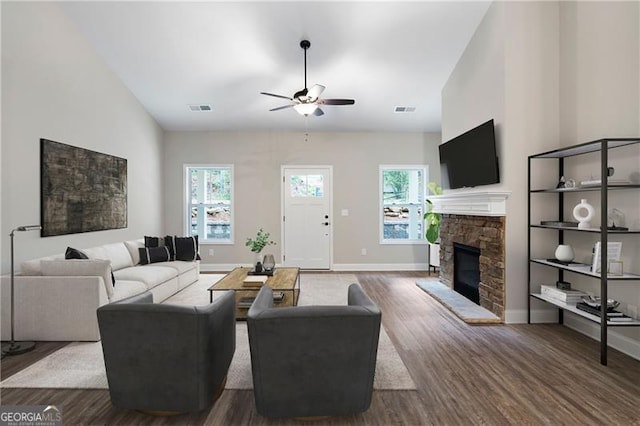 living area with a stone fireplace, plenty of natural light, wood finished floors, and visible vents