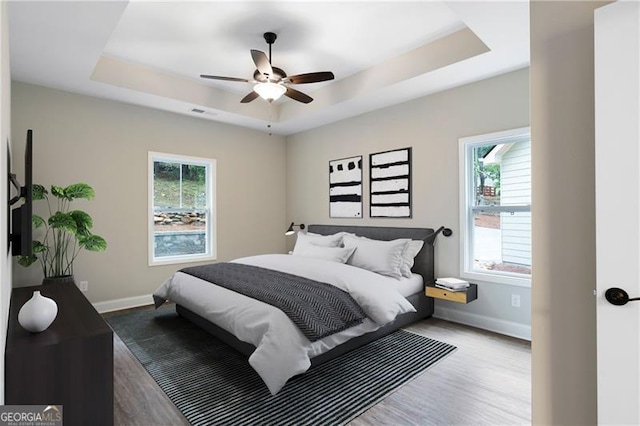 bedroom with visible vents, a raised ceiling, wood finished floors, baseboards, and ceiling fan