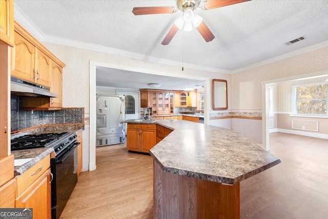 kitchen with light wood-type flooring, tasteful backsplash, ornamental molding, black gas range, and a center island