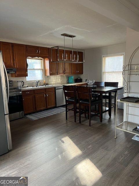 kitchen with appliances with stainless steel finishes, backsplash, dark wood-type flooring, sink, and pendant lighting