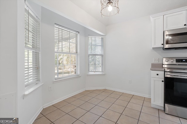 kitchen featuring white cabinets, appliances with stainless steel finishes, light tile patterned floors, and a chandelier