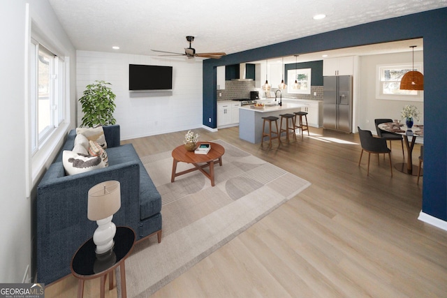 living room featuring a textured ceiling, ceiling fan, light wood-type flooring, and sink