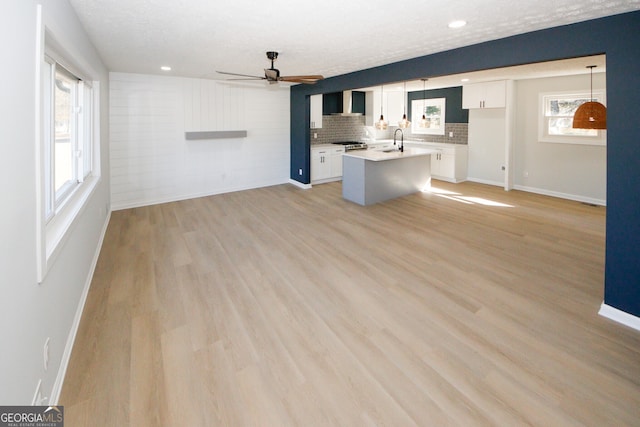 kitchen featuring light wood-type flooring, sink, wall chimney range hood, decorative light fixtures, and white cabinets