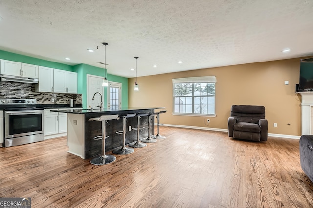 kitchen featuring stainless steel range, light hardwood / wood-style flooring, pendant lighting, a textured ceiling, and a kitchen island with sink