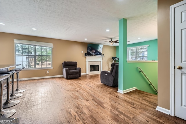 living area featuring ceiling fan, wood-type flooring, and a textured ceiling