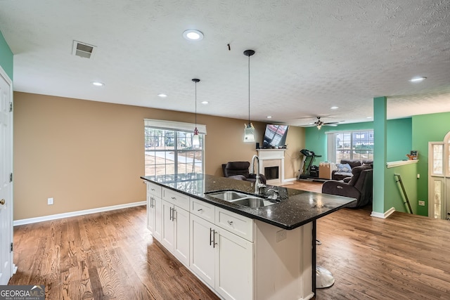 kitchen with a kitchen island with sink, white cabinets, sink, dark stone countertops, and a textured ceiling