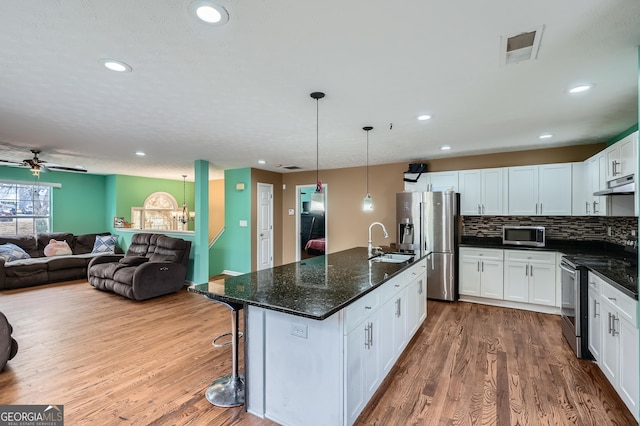 kitchen with dark wood-type flooring, white cabinets, hanging light fixtures, an island with sink, and appliances with stainless steel finishes