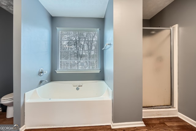 bathroom with hardwood / wood-style floors, plus walk in shower, a textured ceiling, and toilet