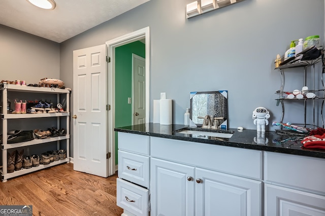 interior space featuring dark stone countertops, white cabinetry, light hardwood / wood-style flooring, and sink